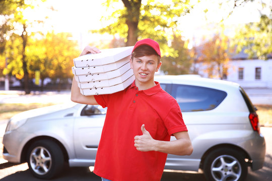 Pizza delivery boy holding boxes with pizza near car