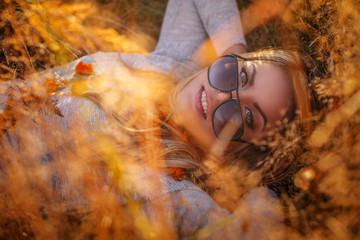 Young blond woman in sunglasses lying in golden grass.