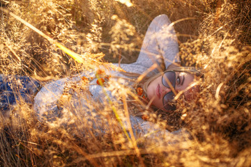 Young blond woman in sunglasses lying in golden grass.