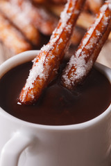 Traditional churros dipped in a cup of chocolate macro. vertical
