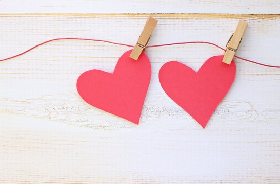 Couple of pink paper hearts pinned on twine, white wooden wall background. Romantic DIY ideas and home decor.