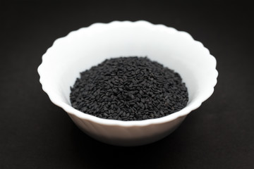 Organic Black Sesame (Sesamum indicum) in white ceramic bowl on dark background.