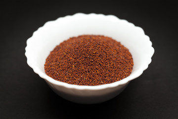 Organic Small Brown Mustard Seeds (Brassica juncea) in white ceramic bowl on dark background.