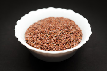 Organic Linseed or Flaxseed (Linum usitatissimum) in white ceramic bowl on dark background.