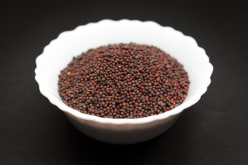 Organic brown mustard (Brassica juncea) in white ceramic bowl on dark background.