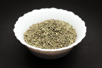 Organic Aniseed (Pimpinella anisum) in white ceramic bowl on dark background.