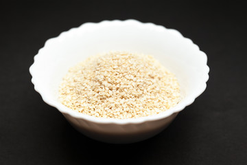 Organic White Sesame (Sesamum indicum) in white ceramic bowl on dark background.
