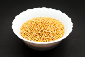 Organic yellow mustard (Brassica alba) in white ceramic bowl on dark background.
