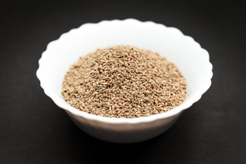Organic Ajwain (Trachyspermum ammi) in white ceramic bowl on dark background.