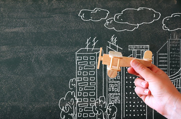 close up photo of woman's hand holding wooden toy airplane against chalkboard with city illustration.success and inspiration concept
