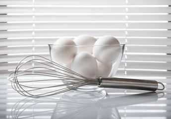 White eggs in bowl and wire whisk