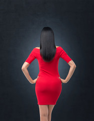 Rear view of gorgeous brunette in red dress posing on black background.