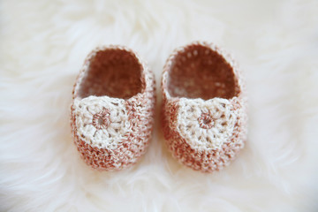 Little baby shoes. Hand knitted first sneakers for newborn  girl. Crochet handmade bootees on fluffy white background.