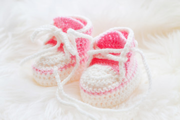 Little baby shoes. Hand knitted first sneakers for newborn  girl. Crochet handmade pink bootees on fluffy white background.