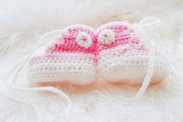 Fototapeta na wymiar Little baby shoes. Hand knitted first sneakers for newborn girl. Crochet handmade pink bootees on fluffy white background.