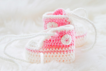 Little baby shoes. Hand knitted first sneakers for newborn  girl. Crochet handmade pink bootees on fluffy white background.