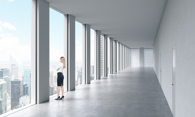 A woman in formal clothes is looking out the window. Empty modern bright clean interior of an open...