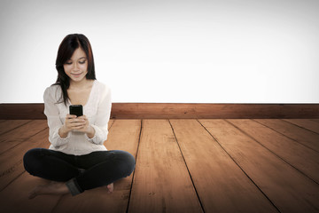 Pretty asian girl using cellphone on the wooden floor