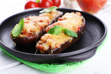 Dish of eggplant with cherry tomatoes and cheese in black pan on wooden table, closeup