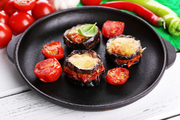Dish of eggplant with cherry tomatoes and cheese in black pan on wooden table, closeup