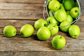 Ripe green apple in metal bucket on wooden table close up