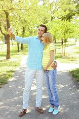 Obraz premium Young pregnant woman with husband making selfie in park