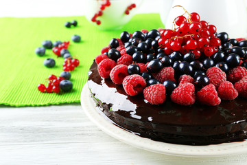 Delicious chocolate cake with summer berries on wooden table with green napkin, closeup