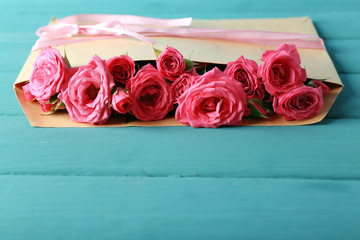 Beautiful roses in envelope on wooden background