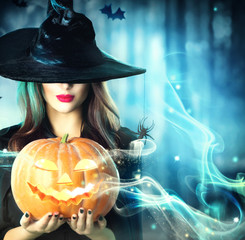 Halloween witch with a magic pumpkin in a dark forest