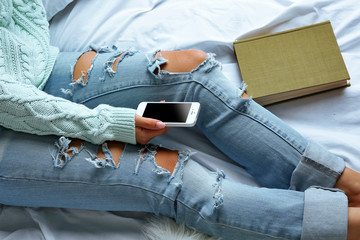 Woman in blue jeans watching phone on bed top view point