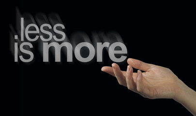 Sharing a less is more philosophy - Female hand appearing to release a phrase LESS IS MORE on a...