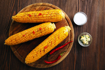 Grilled corn with hot pepper on rustic round plate on wooden background