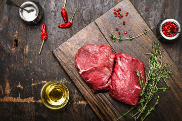 Meat steaks on rustic cutting board with thyme, oil and spices.