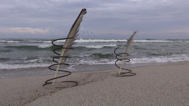  Seascape with two metal springs with two feathers inside stuck in the sand