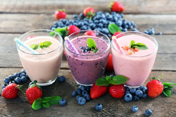 Tasty blueberry, strawberry and milk yogurts in a row decorated with berries and mint on wooden background
