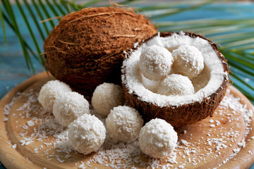 Candies in coconut flakes and fresh coconut on color wooden background