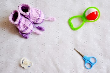 Collection of baby things: booties, pacifier, scissors, rattle on white background. Top view.