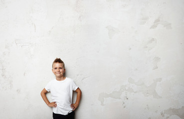 Young boy wearing white tshirt and smiling on the concrete wall