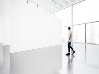 Empty gallery interior with white canvas and young man.  - obrazy, fototapety, plakaty