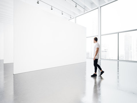 Empty gallery interior with white canvas and young man. 