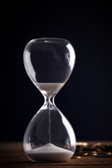 Hourglass and coins on wooden table on black background