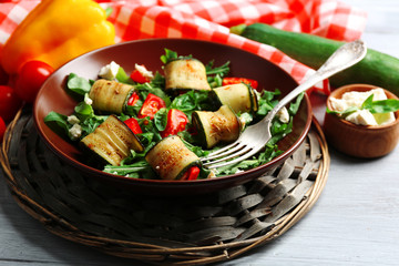 Salad with arugula and zucchini rolls on plate, on table background