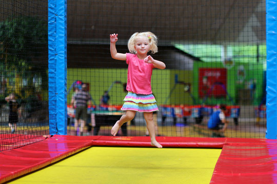 Little child jumping at trampoline in indoors playground. Active toddler girl having fun at sport centre.