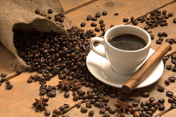 Coffee cup with coffee beans, cigar, cinnamon  on bagging on wood.
