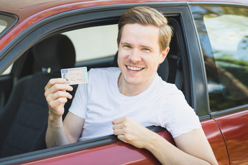 Junger Mann sitzt im Auto und zeigt seinen Führerschein - obrazy, fototapety, plakaty