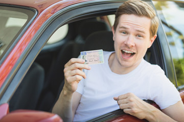 Junger Mann sitzt im Auto und zeigt seinen Führerschein