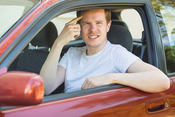 Junger Mann sitzt im Auto und zeigt den Mittelfinger / Vogel