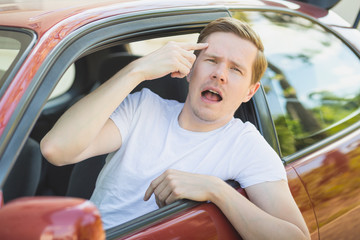 Junger Mann sitzt im Auto und zeigt den Mittelfinger / Vogel