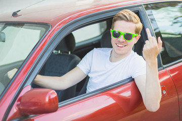 Naklejka premium Junger Mann mit Sonnenbrille sitzt im Auto und zeigt Mittelfinge