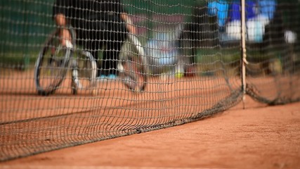 Wheelchair tennis player is seen behind the tennis net on a clay court - Powered by Adobe